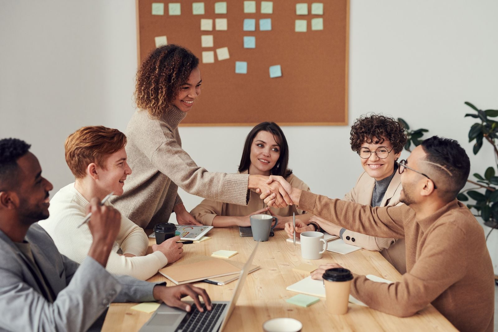 Colegas apertando as mãos à mesa de reunião, cena de convivência para explicar o que é inteligência emocional no trabalho