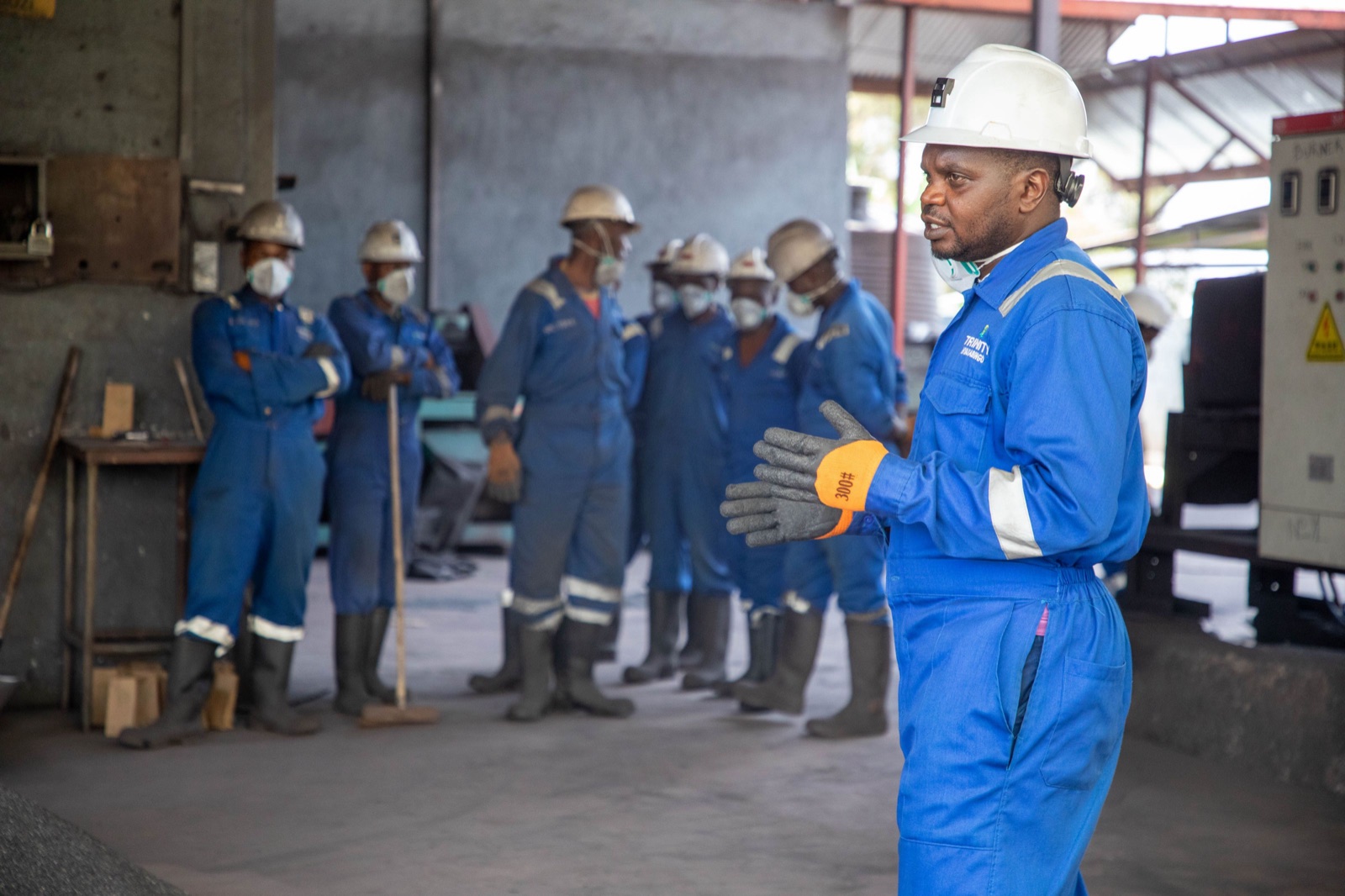 Líder de segurança conduzindo um treinamento para equipe de operários de capacete e uniforme em ambiente industrial, como em uma palestra de SIPAT